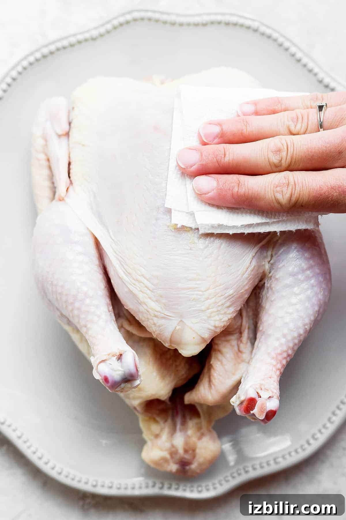 Patting chicken skin dry with a paper towel.