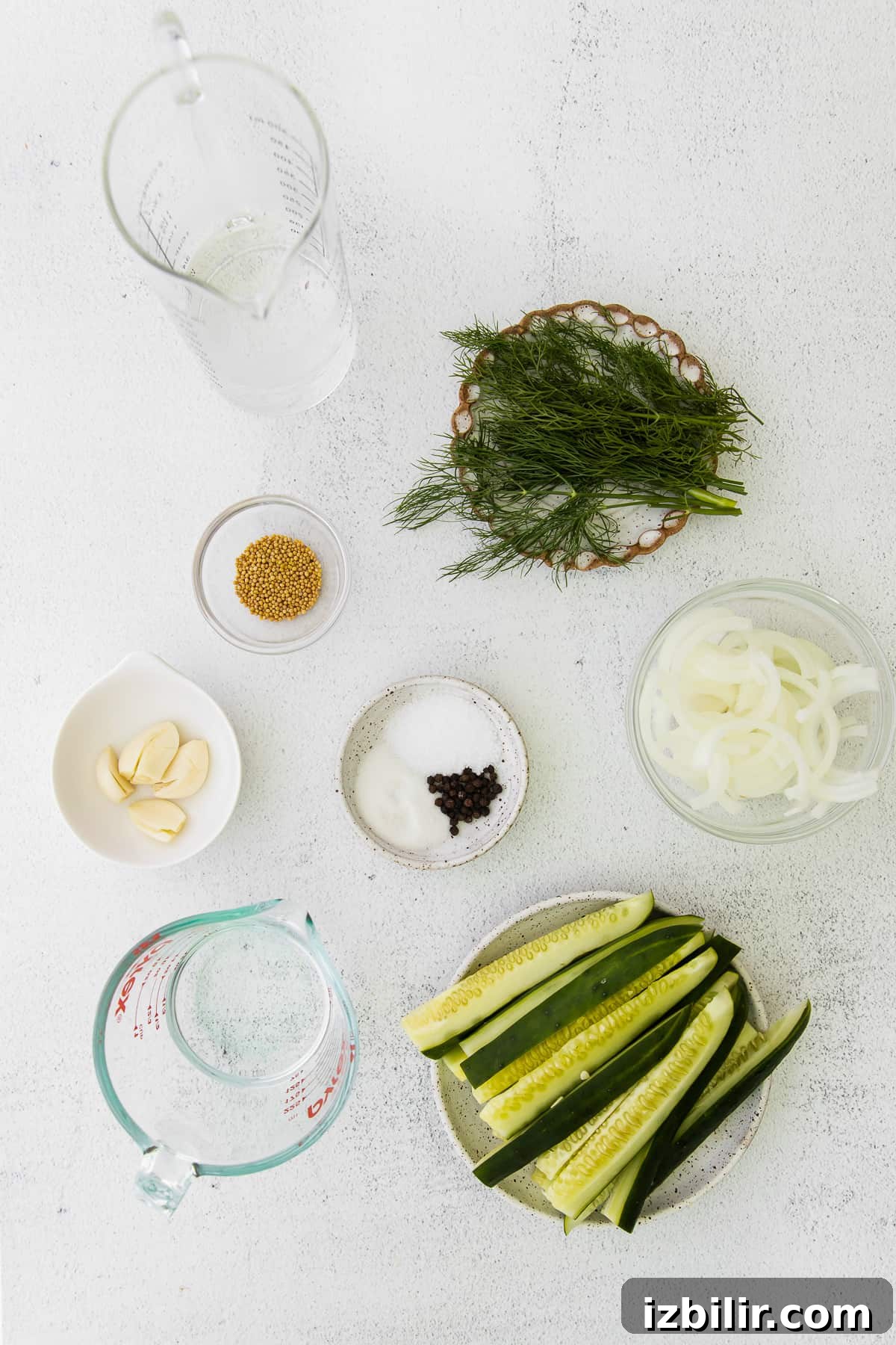 Sliced cucumbers, fresh dill, white onion, mustard seeds, sugar, garlic, and vinegar on the counter top. 