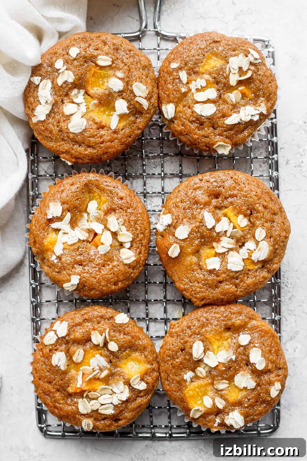 Seriously yummy peach muffins! This peach muffin recipe is made with 100% whole grains and uses juicy fresh peaches for incredible flavor. peach muffins on a cooling rack topped with rolled oats