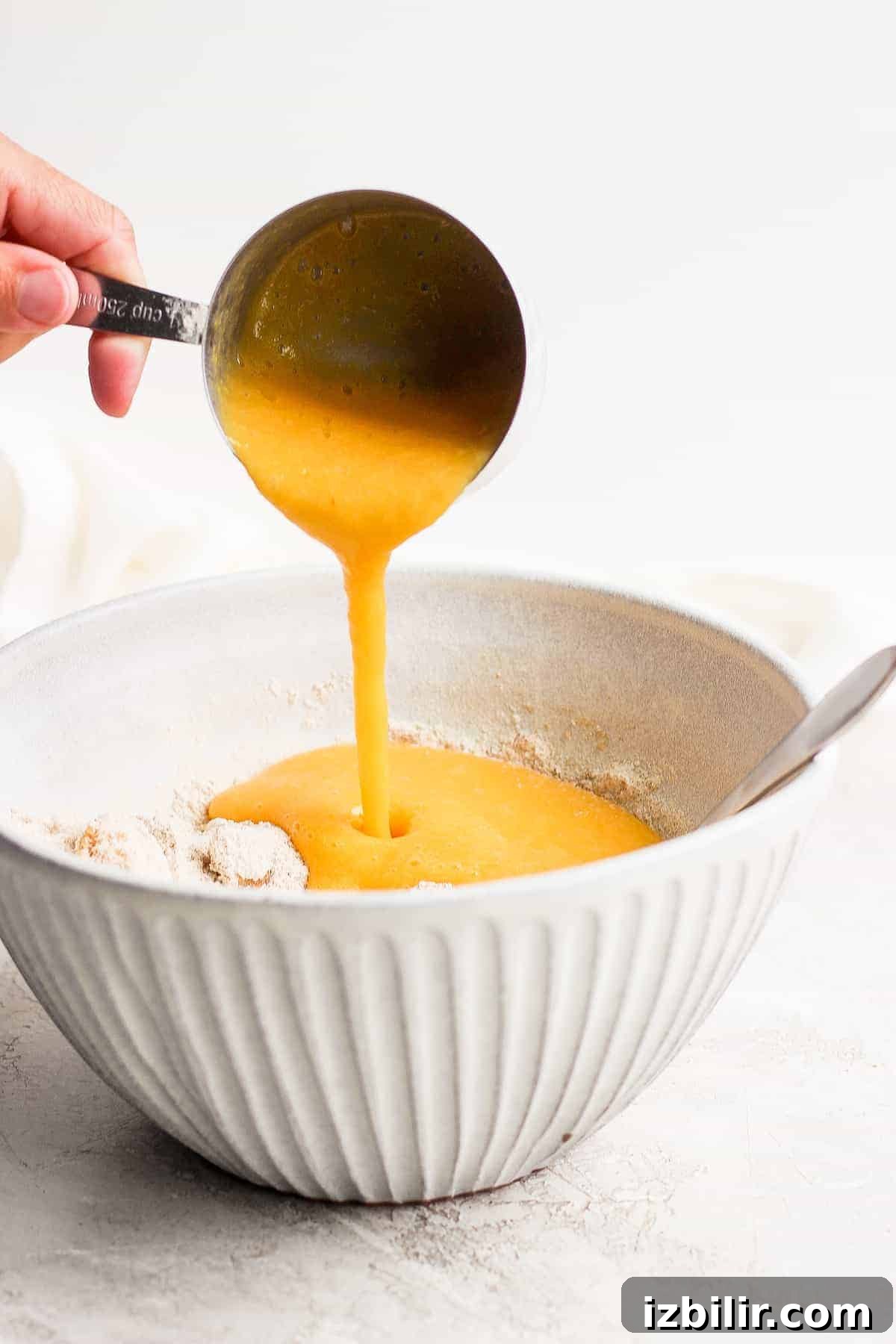 Adding peach puree to muffin batter. pureed peaches being poured in a bowl with the rest of the peach muffin ingredients