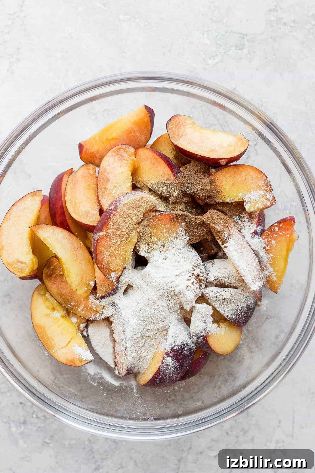 Sliced peaches tossed with flour and spices. Sliced peaches in a bowl topped with flour and spices.