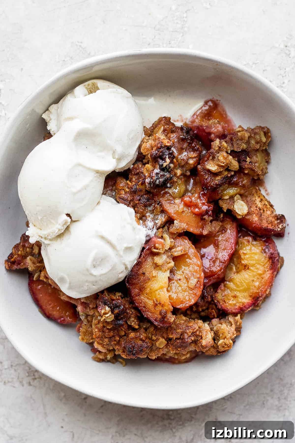 Serve peach crisp with ice cream. Peach crisp in a bowl with vanilla ice cream.