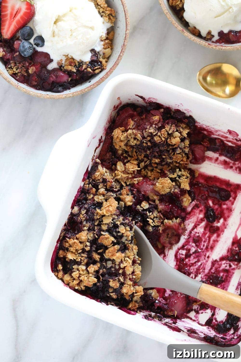 Triple berry crisp made with blueberries, strawberries, raspberries, and a crumbled oat topping. berry crumble in a white dish with serving spoon