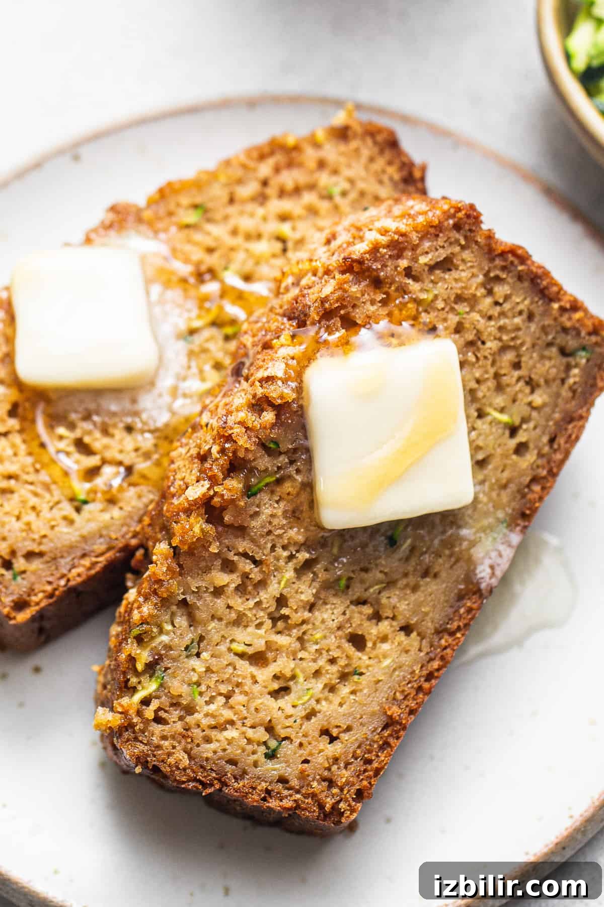 Moist Zucchini Bread with Cinnamon and Walnuts 2 Two slices of zucchini bread with butter on a plate.