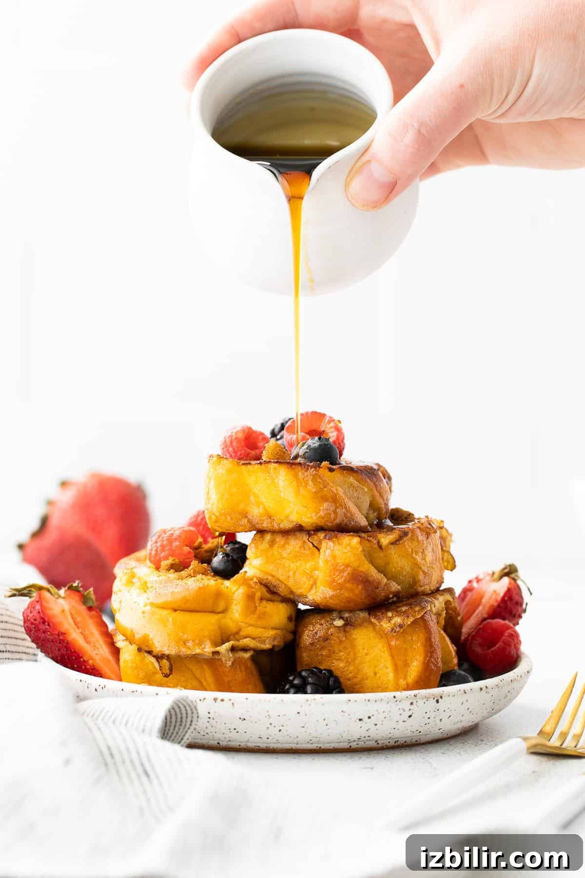 maple syrup being poured over slices of french toast topped with berries