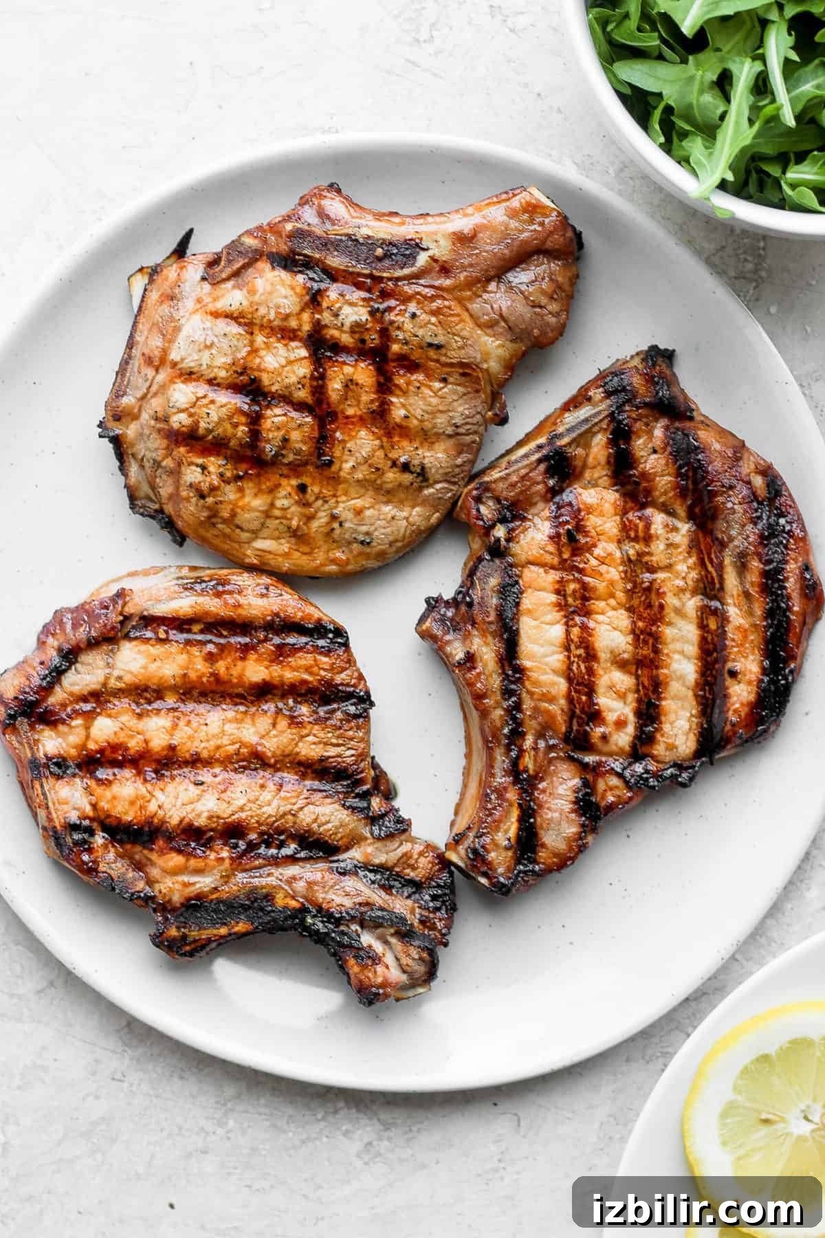 This grilled pork chops recipe comes out so juicy and tender on the inside and has gorgeous, charred grill marks on the outside. 3 grilled pork chops on plate.