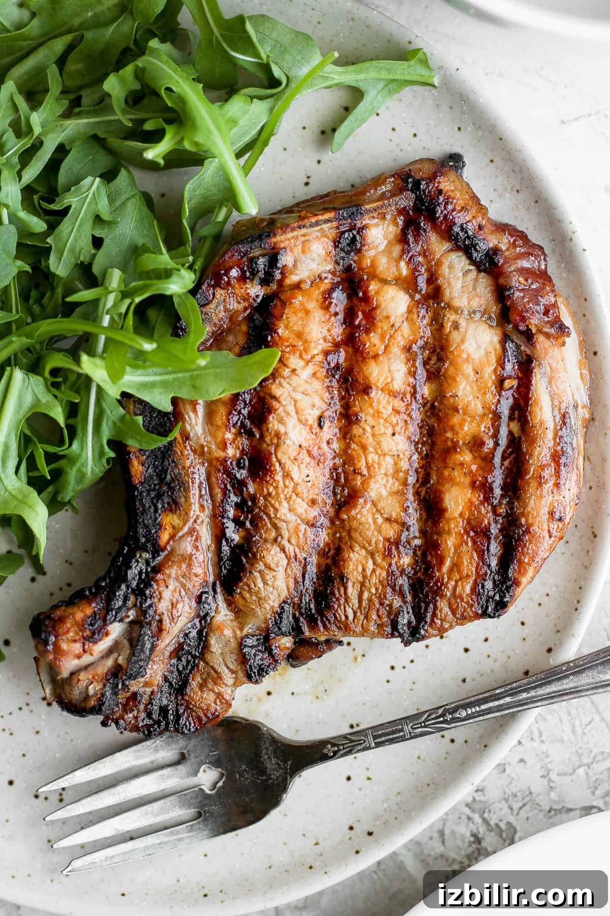 These grilled pork chops are sweet and savory and so juicy! Learn how to grill pork chops perfectly every time with this delicious recipe. grilled pork chop on plate.