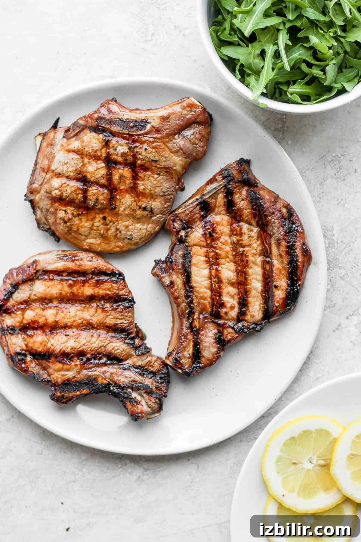 These grilled pork chops are sweet and savory and so juicy! Learn how to grill pork chops perfectly every time with this delicious recipe. grilled pork chops on plate next to arugula.
