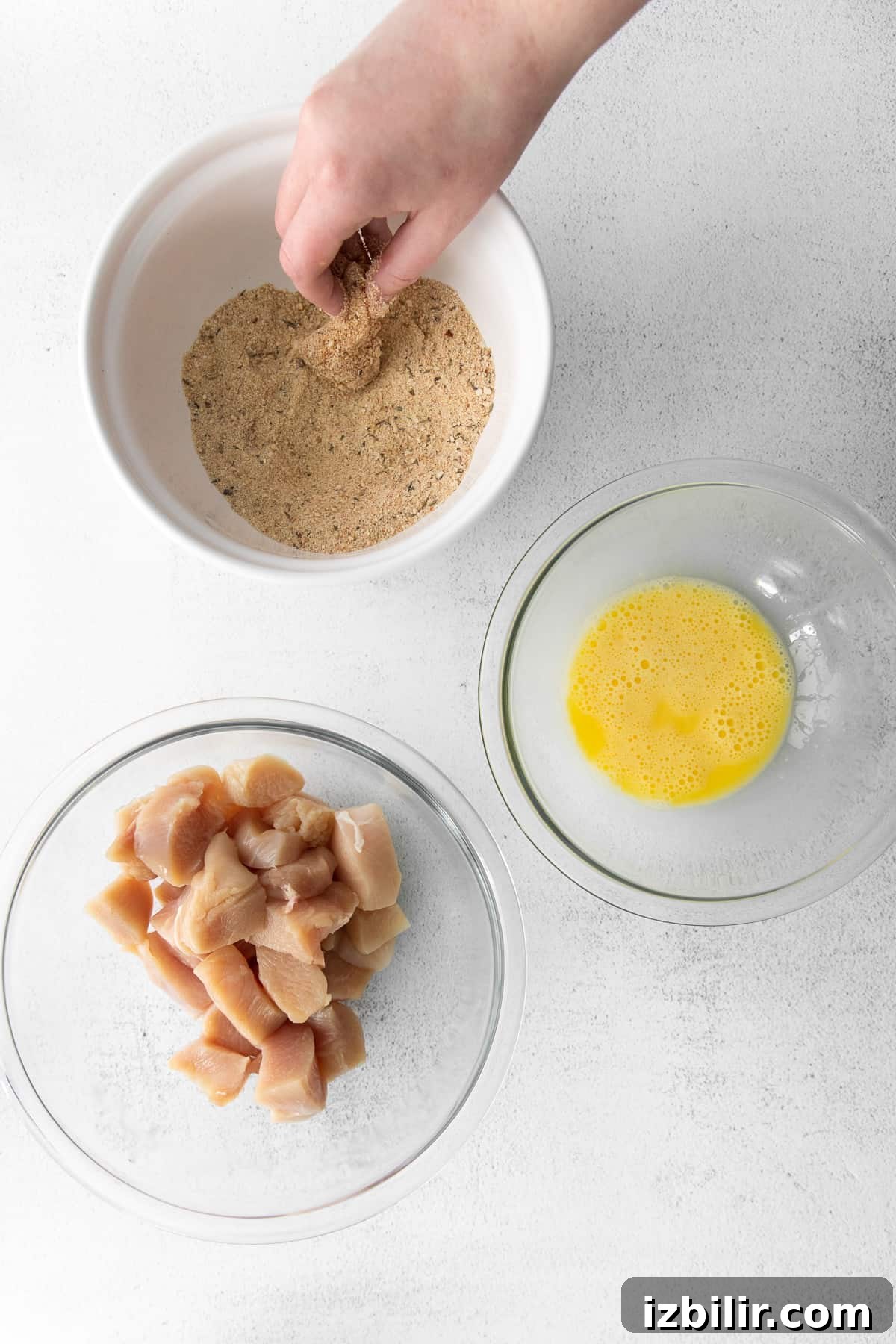 Dipping chicken in bread crumbs.