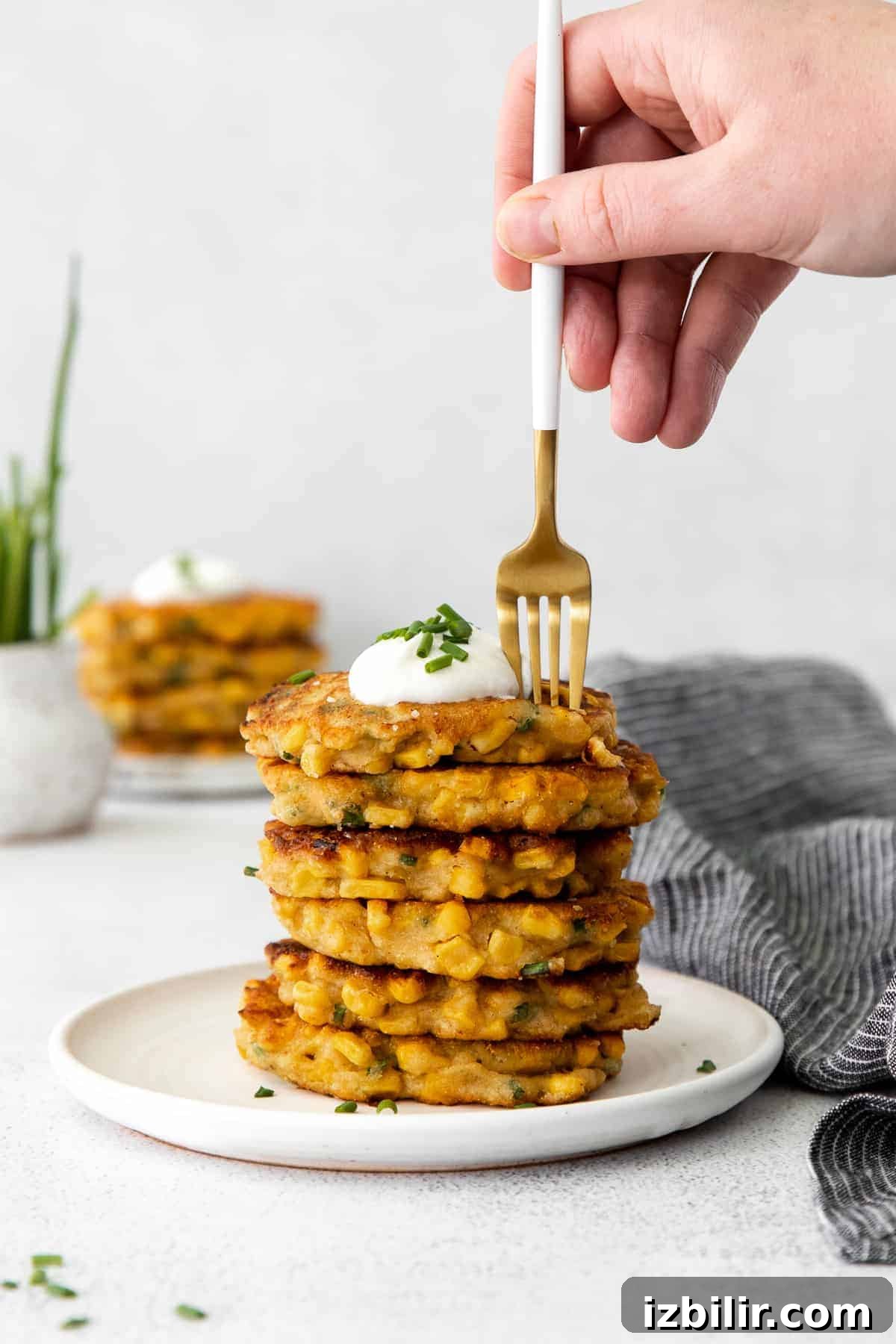 A stack of corn fritters with Greek yogurt and chives sprinkled on top. 
