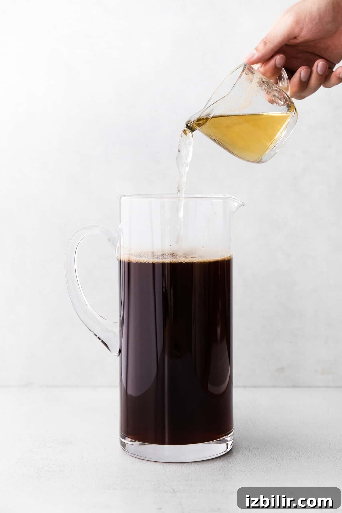 Simple syrup being poured into a pitcher of iced tea