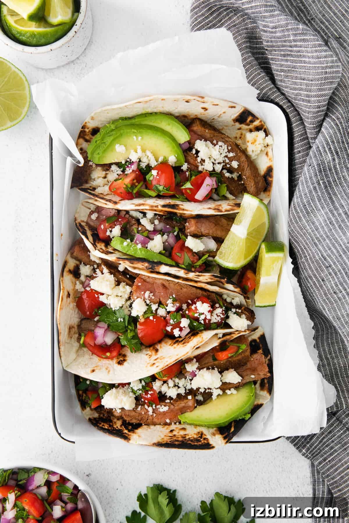 These easy steak tacos are made from perfectly seasoned sliced flank steak and topped with a simple tomato pico, avocado slices and cotija cheese. Enjoy! steak tacos topped with sliced avocado and cotija cheese