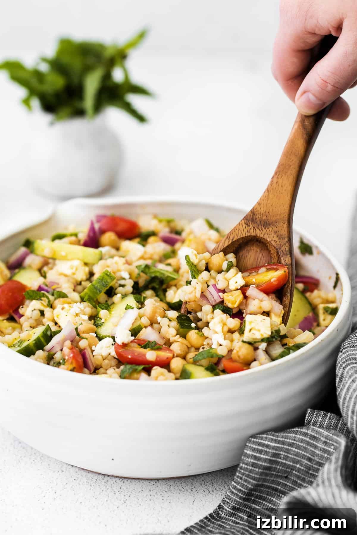 mediterranean couscous salad in a bowl being stirred with a spoon