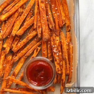 Baked sweet potato fries on a baking sheet with ketchup.