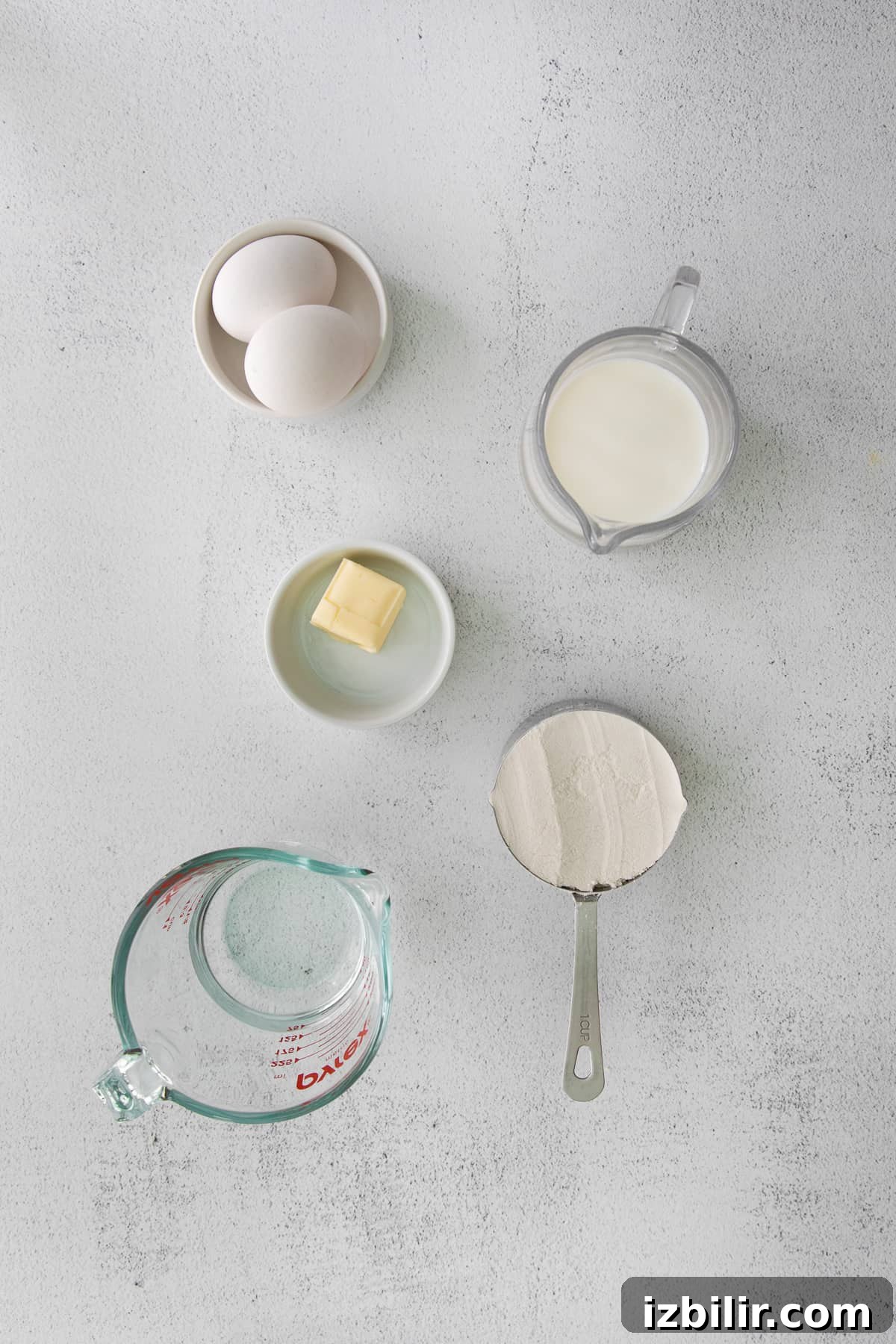 Milk, flour, butter, eggs, and water in small dishes.