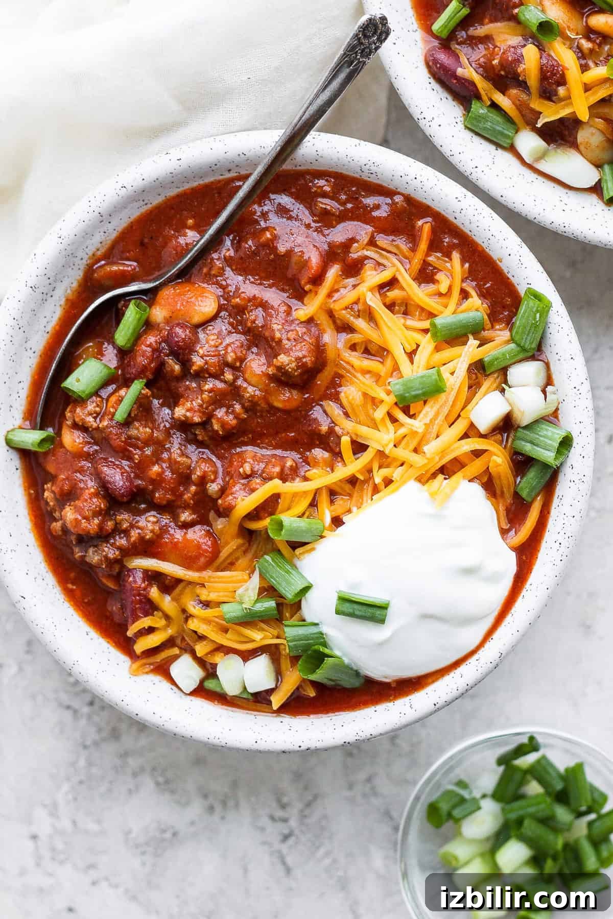 Slow cooker chili in a bowl topped with sour cream, shredded cheese and diced green onion.