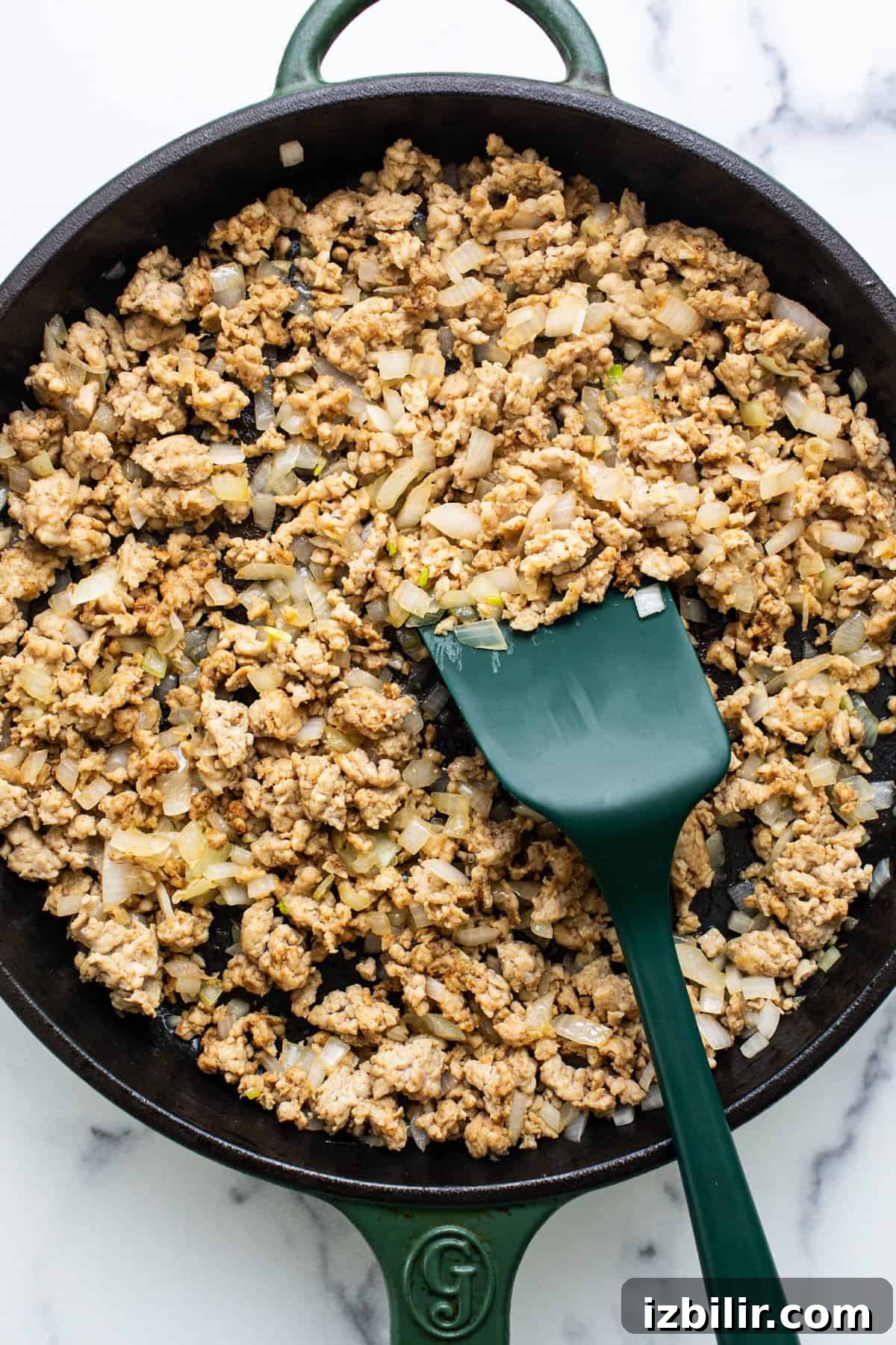 Light Enchilada Dip Recipe with Black Beans and Cheese 3 Ground meat cooked with diced onions in a cast iron skillet, with a green spatula.