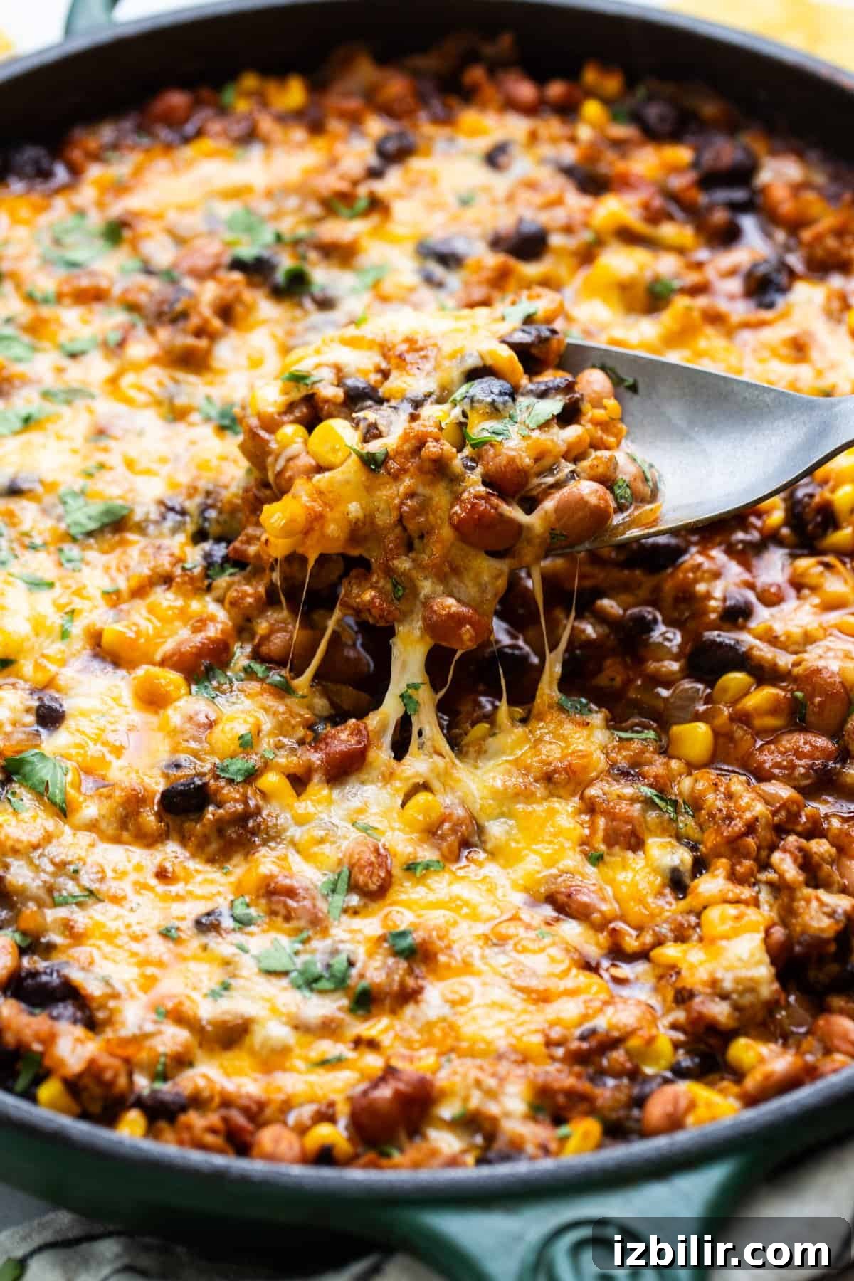 Light Enchilada Dip Recipe with Black Beans and Cheese 5 Skillet of baked cheesy chili with a spoon lifting a portion showing melted cheese stretch.