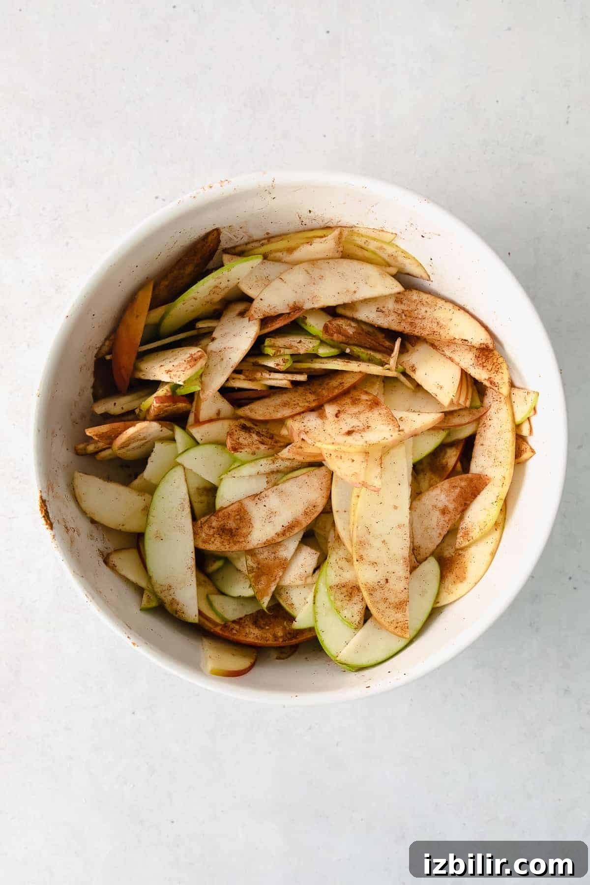 Classic French Apple Tart with Caramelized Apples 4 Apples in a bowl with warm spices mixed in.