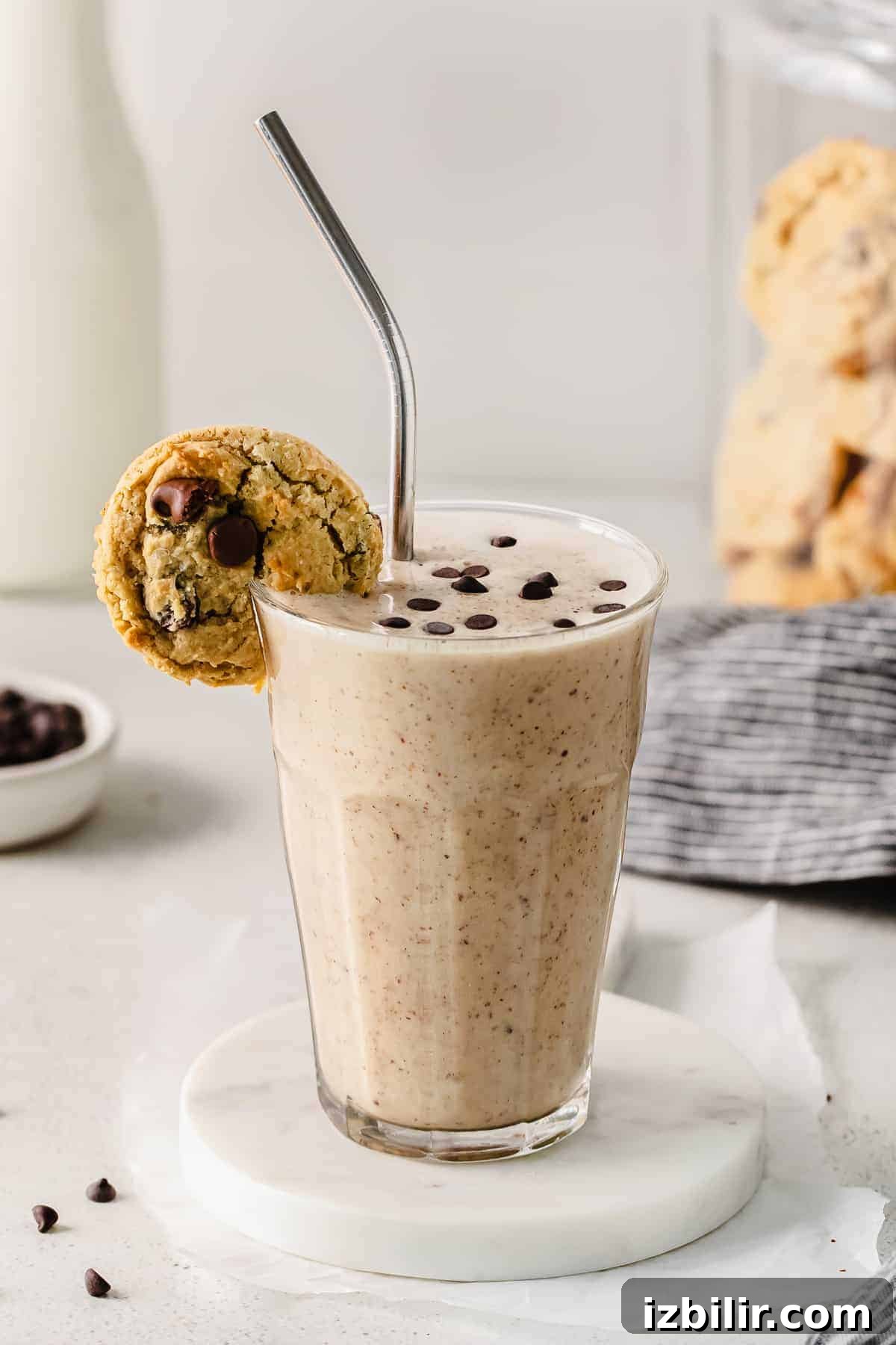 Cookie dough smoothie in a glass with a chocolate chip cookie on the rim. 