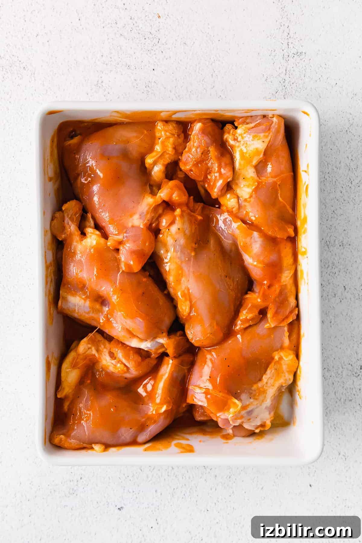 raw boneless chicken thighs in a casserole dish with buffalo sauce