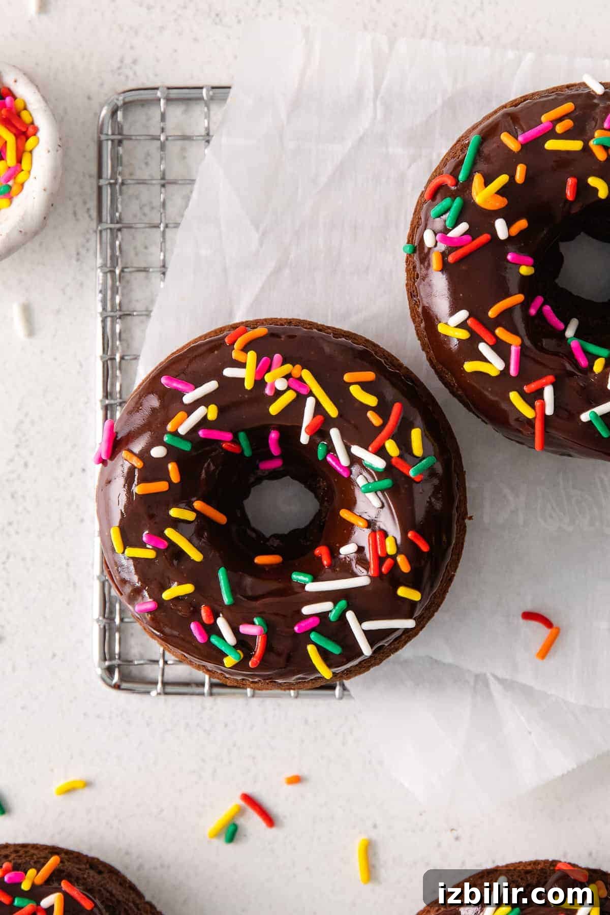 These tender chocolate baked donuts are baked in the oven and never fried. They're perfectly tender and topped with a yummy chocolate frosting and sprinkles. donut on wire rack