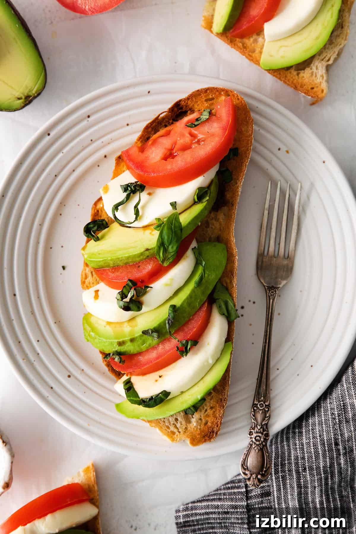 Caprese avocado toast caprese ingredients on top of avocado toast on a plate