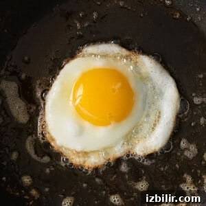 How to Fry an Egg for a Runny Yolk and Crispy Edges 6 A fried egg being cooked in a skillet.