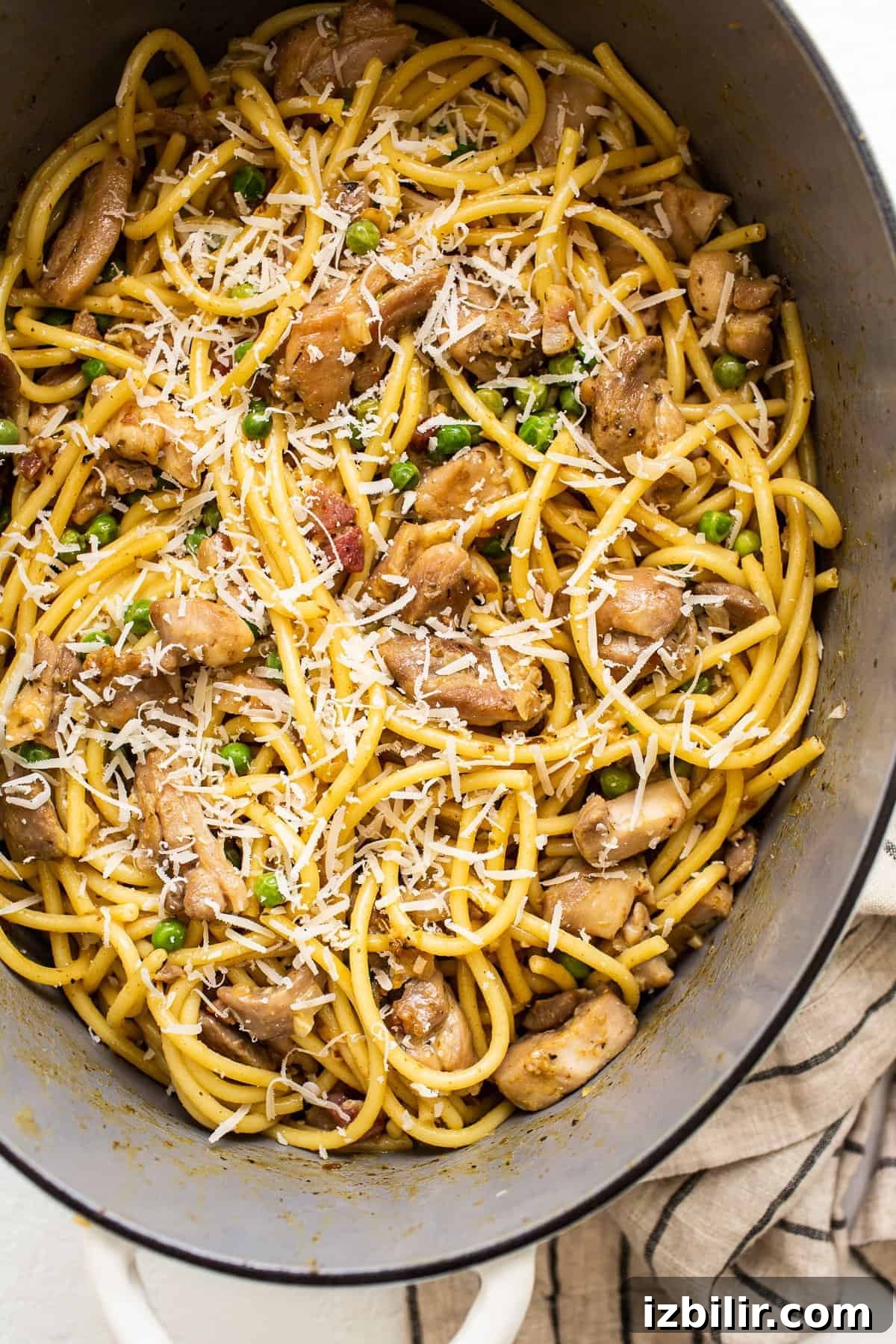Chicken carbonara in a dutch oven topped with shredded parmesan.