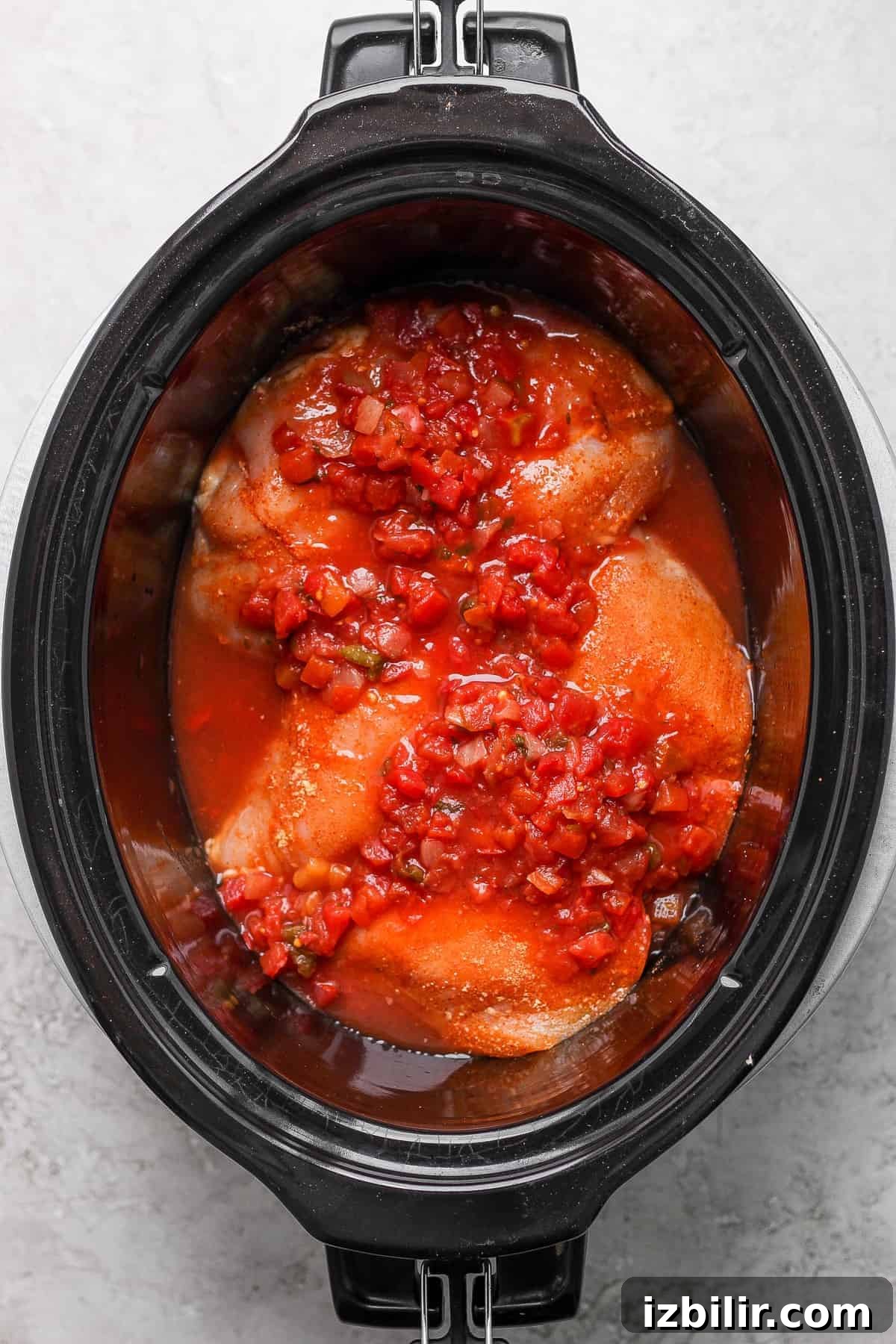Chicken covered in salsa ready to cook in the slow cooker. chicken breast covered in salsa in slow cooker.