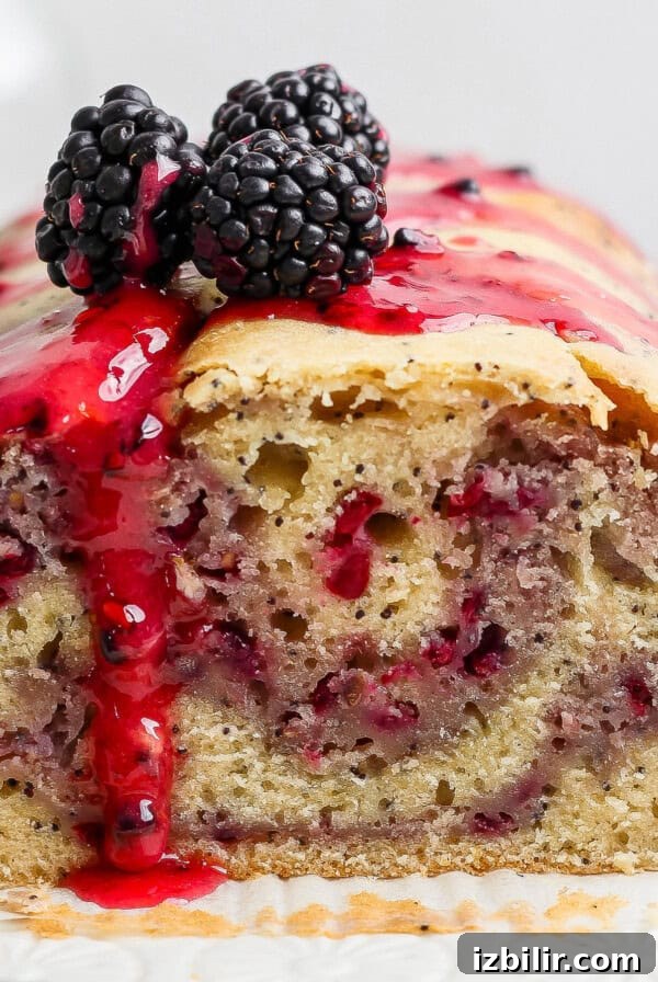 A loaf of blackberry bread with a slice cut, topped with blackberry sauce and fresh blackberries.