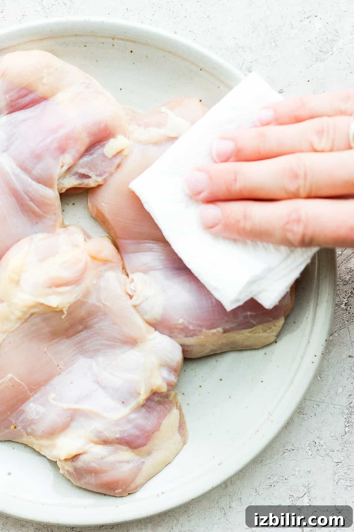 Pat chicken thighs dry before seasoning. Removing moisture from thighs on plate.