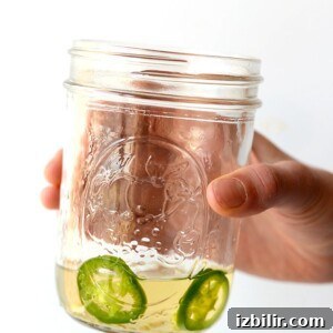 A hand holding a jar of tequila with jalapeño slices in it.