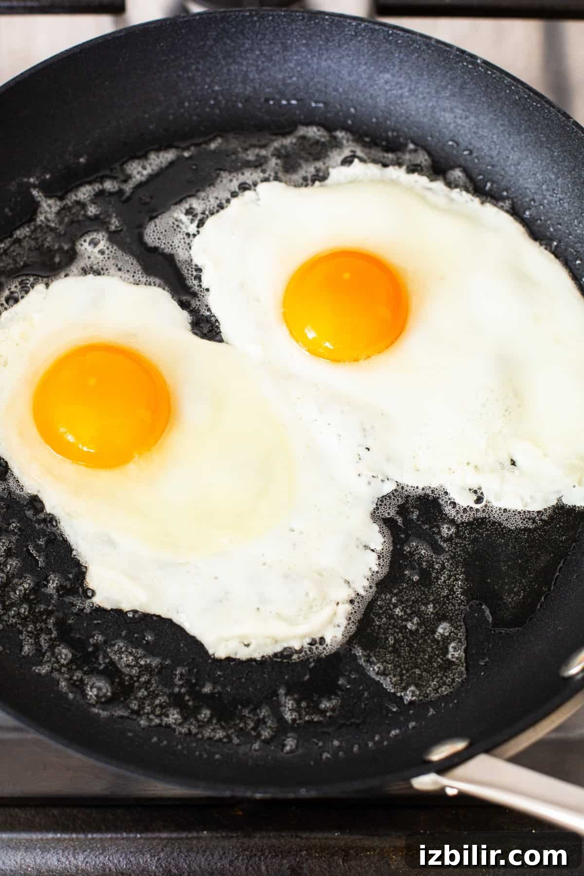 Eggs frying in a skillet to over medium.