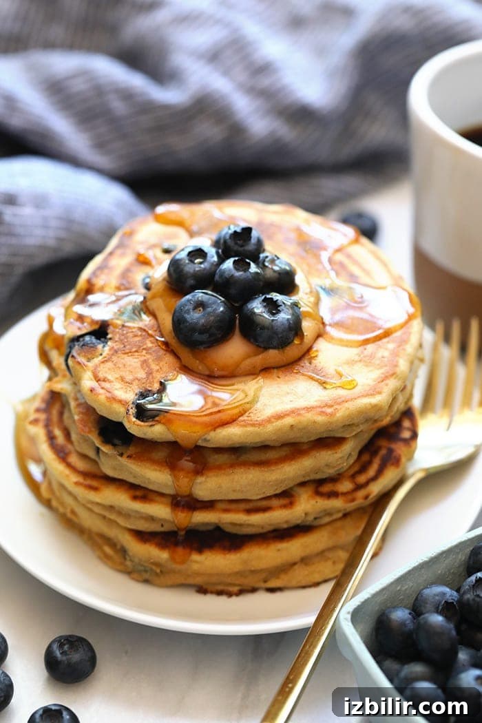 A stack of blueberry pancakes on a plate with a cup of coffee.