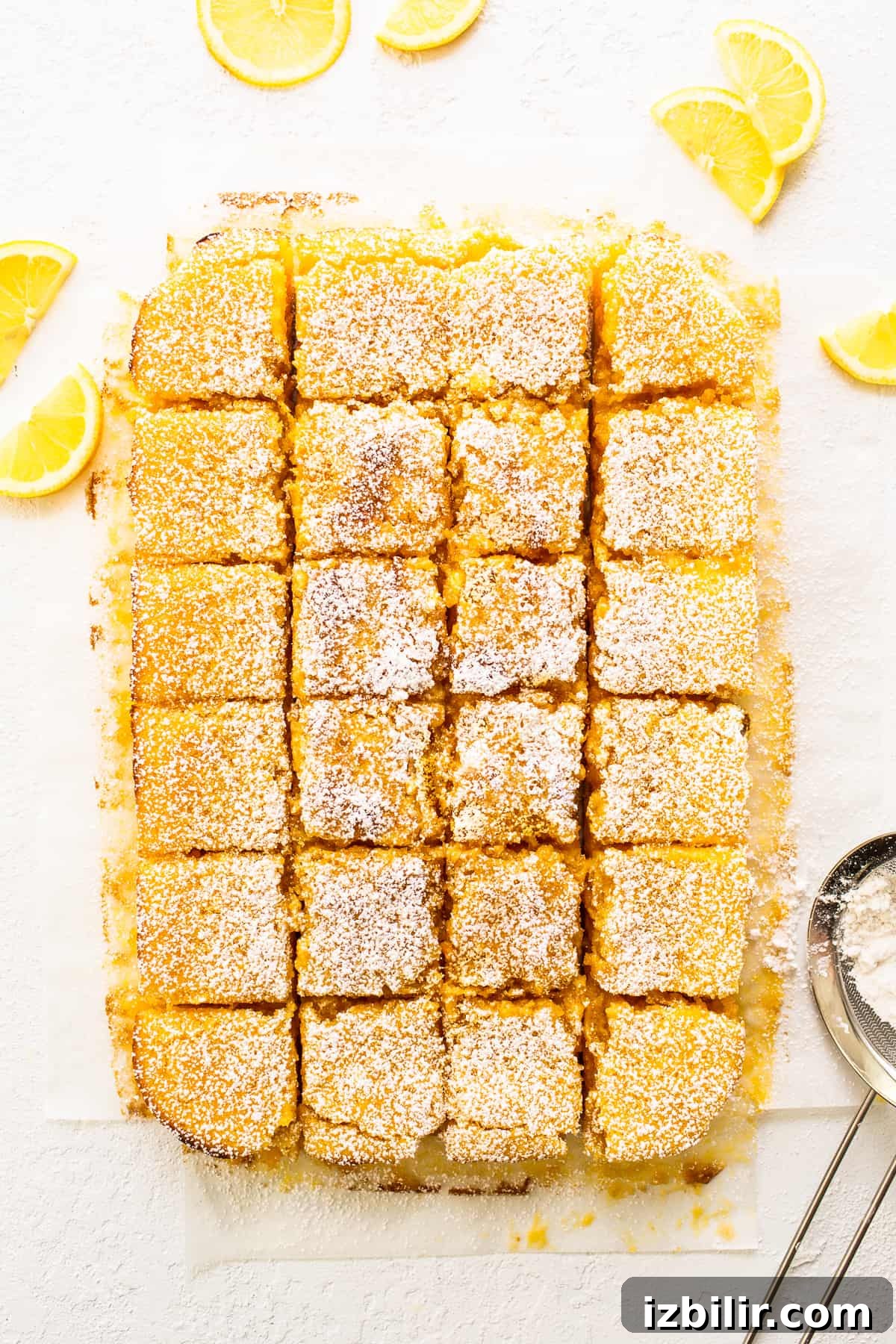 Sliced lemon bars lemon bars on cutting board with lemon wedges.