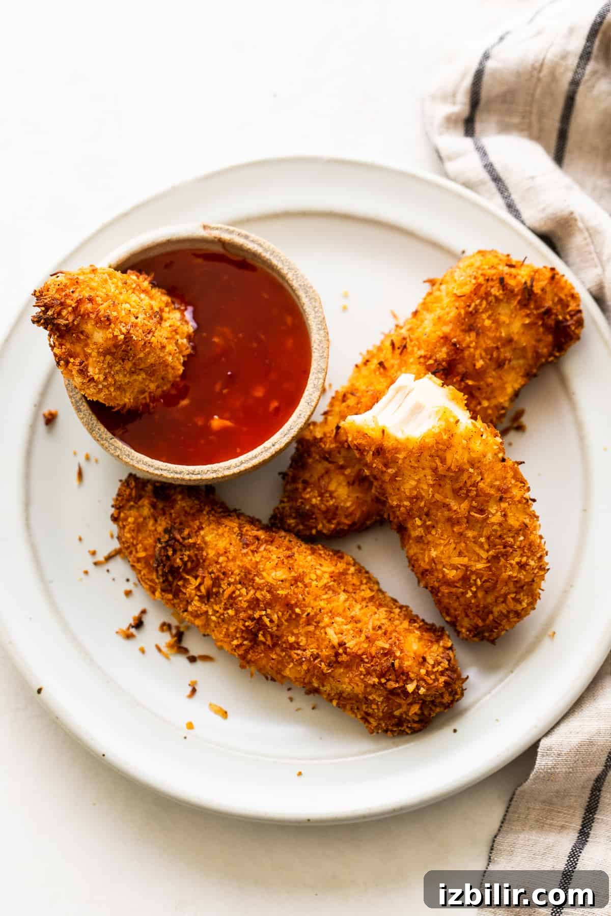 Crispy coconut chicken tenders on a plate with a dipping sauce.