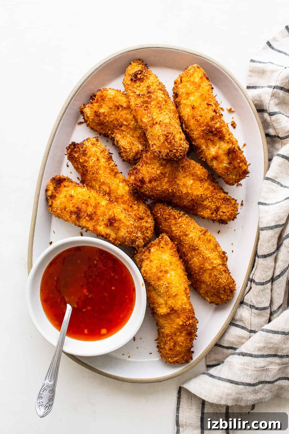 Air fryer coconut chicken tenders on a plate with sweet chili sauce.