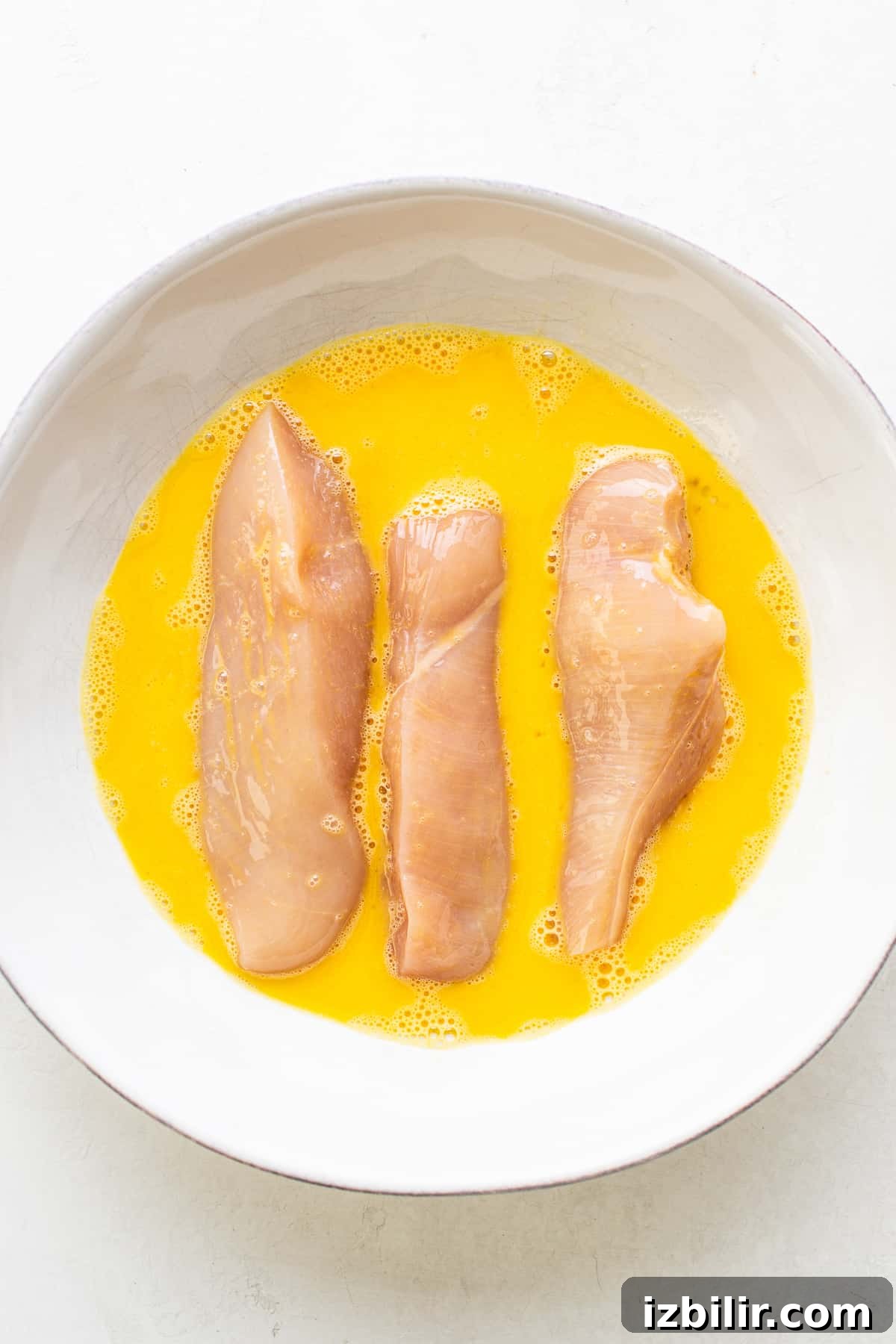 Raw chicken tenders in an egg wash.