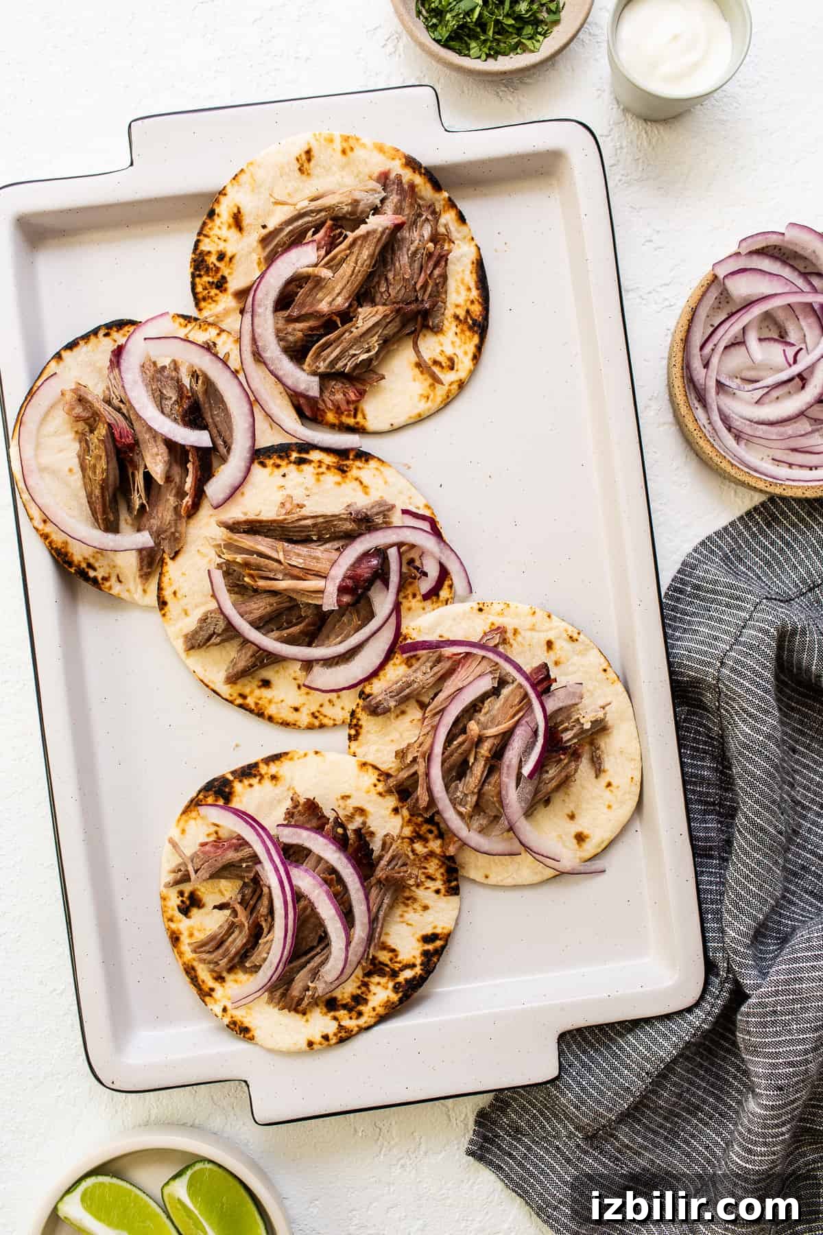 These smoked pulled pork tacos are made with our incredible, fall-off-the-bone smoked pork shoulder and all the best toppings. tortillas with shredded pork and sliced onion on top.