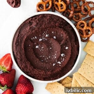 A bowl of edible cookie dough dip next to pretzels and strawberries.