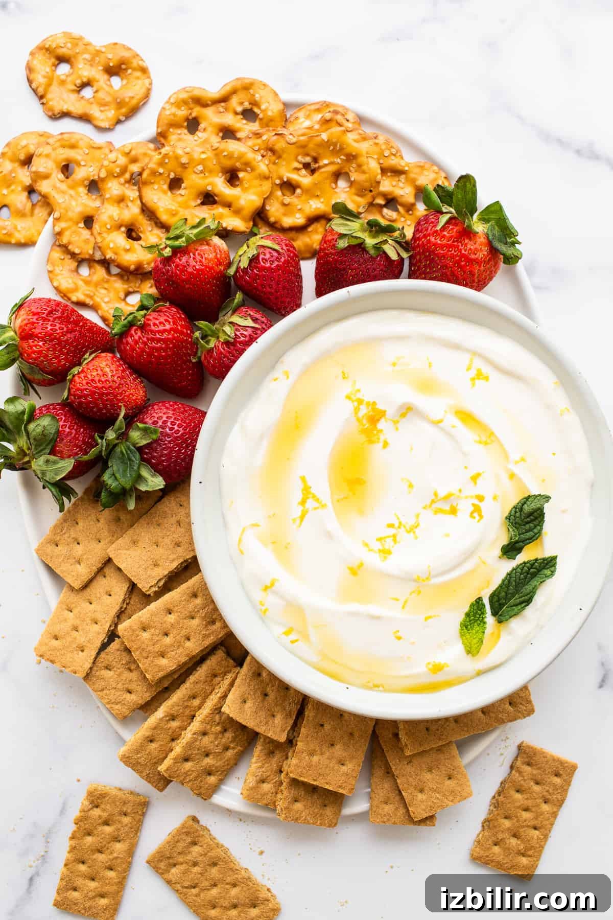 Bowl of fruit dip surrounded by berries, pretzels and graham crackers.
