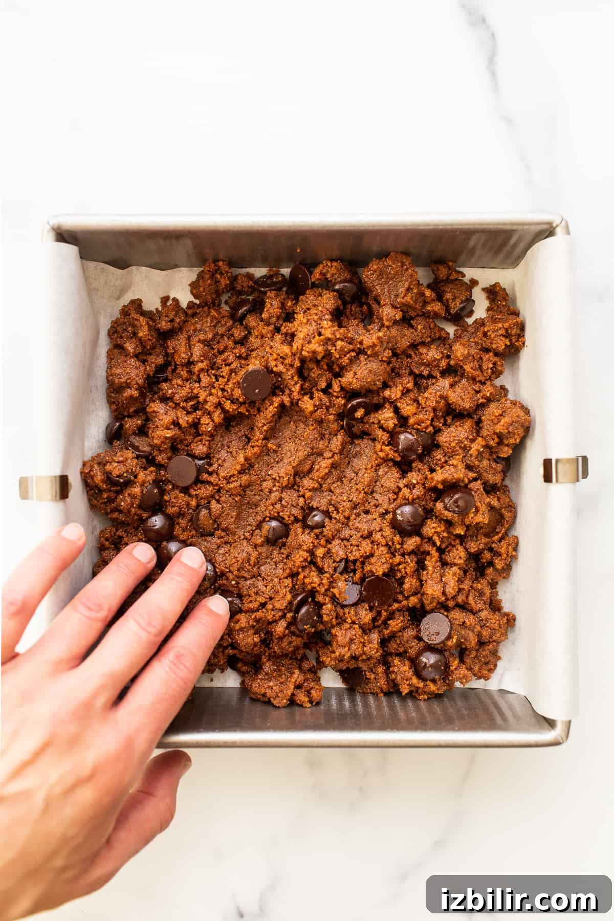 These grain-free chocolate chip cookie bars are made with almond butter, coconut flour, coconut sugar, eggs, and dark chocolate chips! Pressing dough into pan.