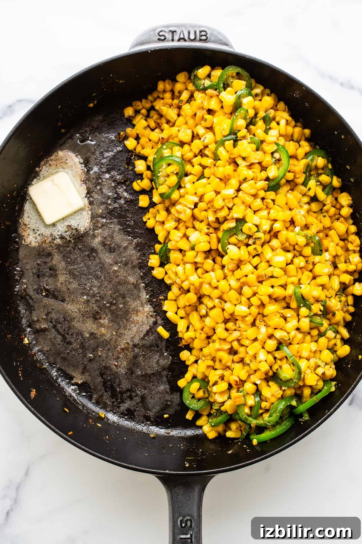Corn and sliced jalapenos in a cast iron skillet. Corn and sliced jalapenos in a cast iron skillet with a pad of melting butter.