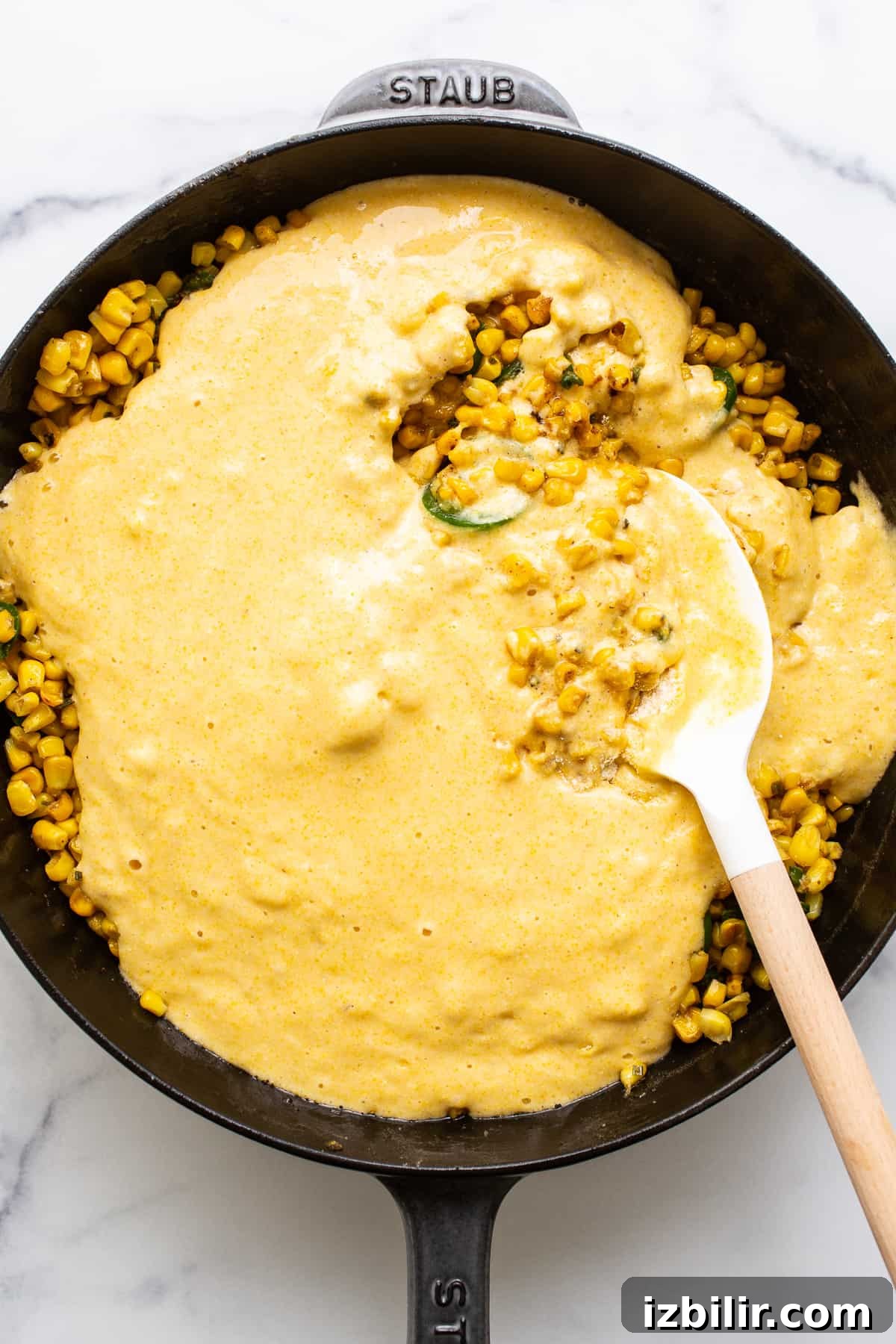 Cornbread mix in a cast iron skillet with corn and jalapenos. Cornbread mix in a cast iron skillet with corn and sliced jalapenos.