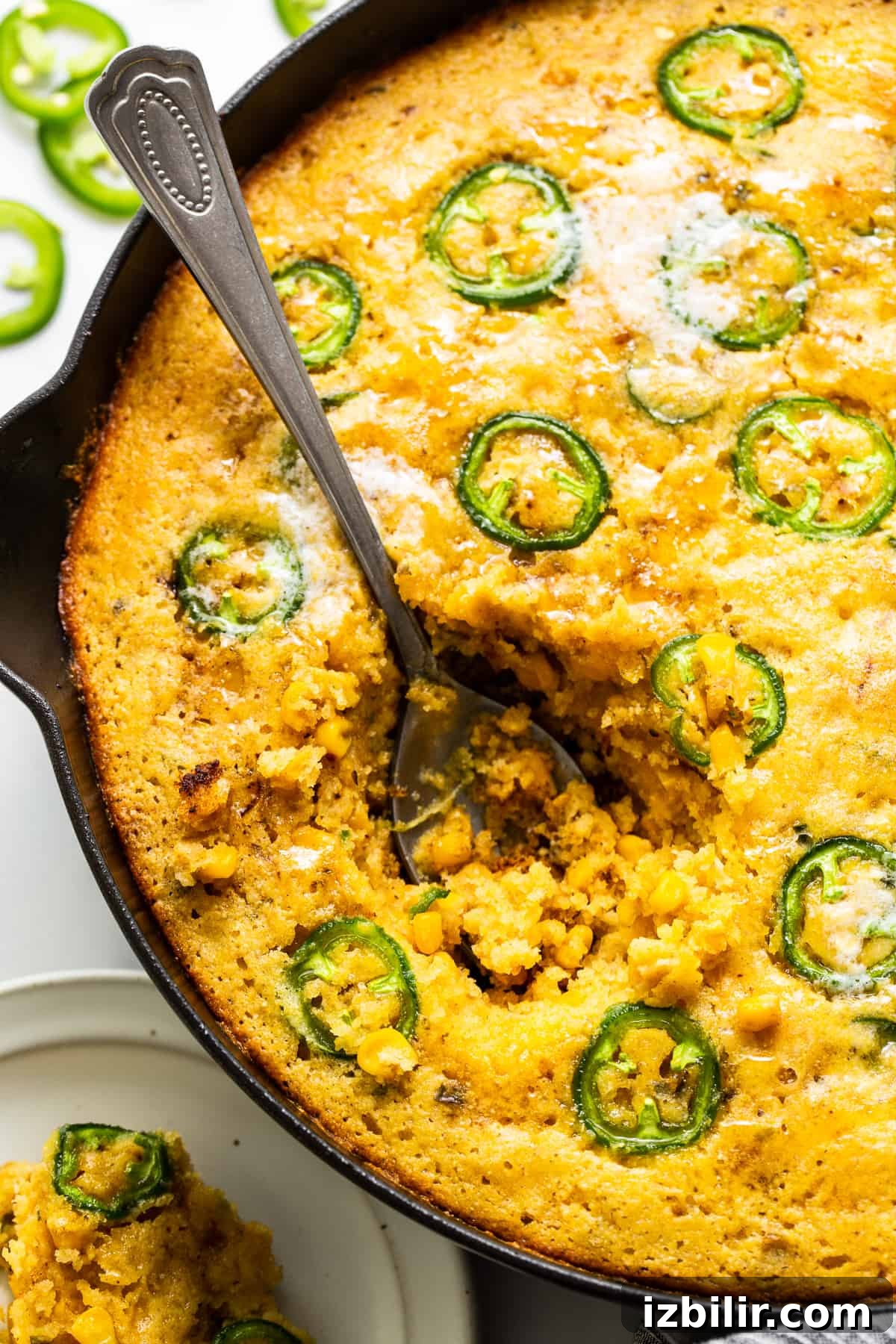 A spoon scooped into a skillet of jalapeño corn pudding. A spoon scooped into a skillet or jalapeno corn pudding.