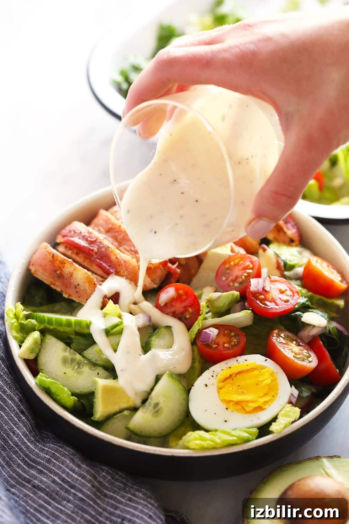This crunchy bacon wrapped chicken salad is packed with veggies, hard boiled eggs, homemade ranch dressing, and flavorful bacon wrapped chicken! pouring dressing onto salad