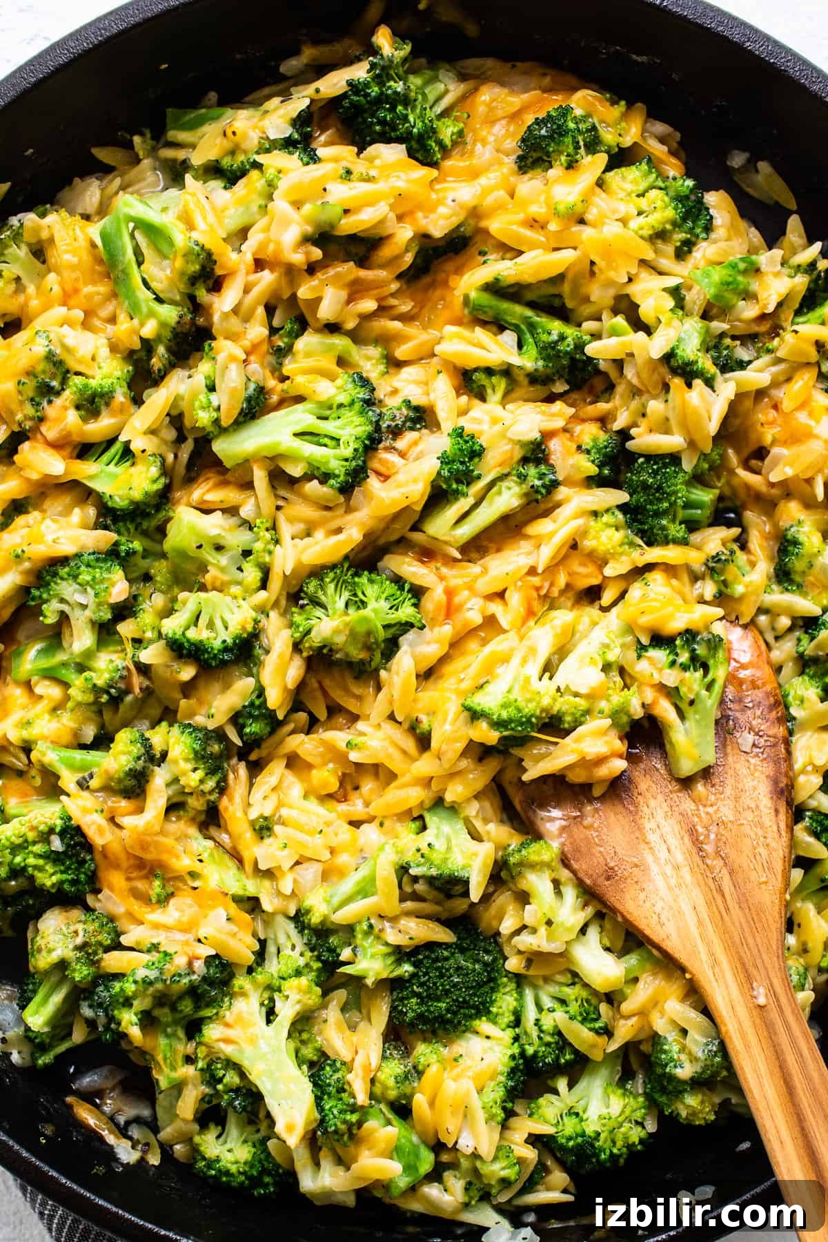 mixing broccoli and cheese with orzo in a cast iron skillet.