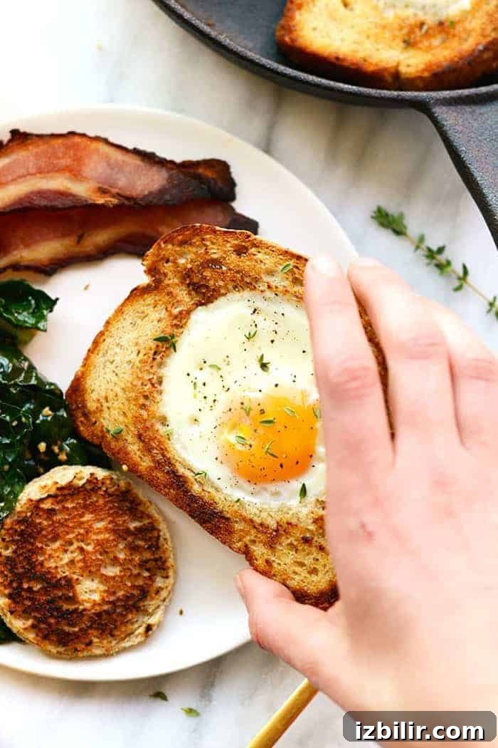 Eggs in a Basket (AKA Egg in a Hole) is such a fun twist on breakfast. Crack your egg right into a piece of toast for an open-face breakfast sandwich! hand holding egg in toast
