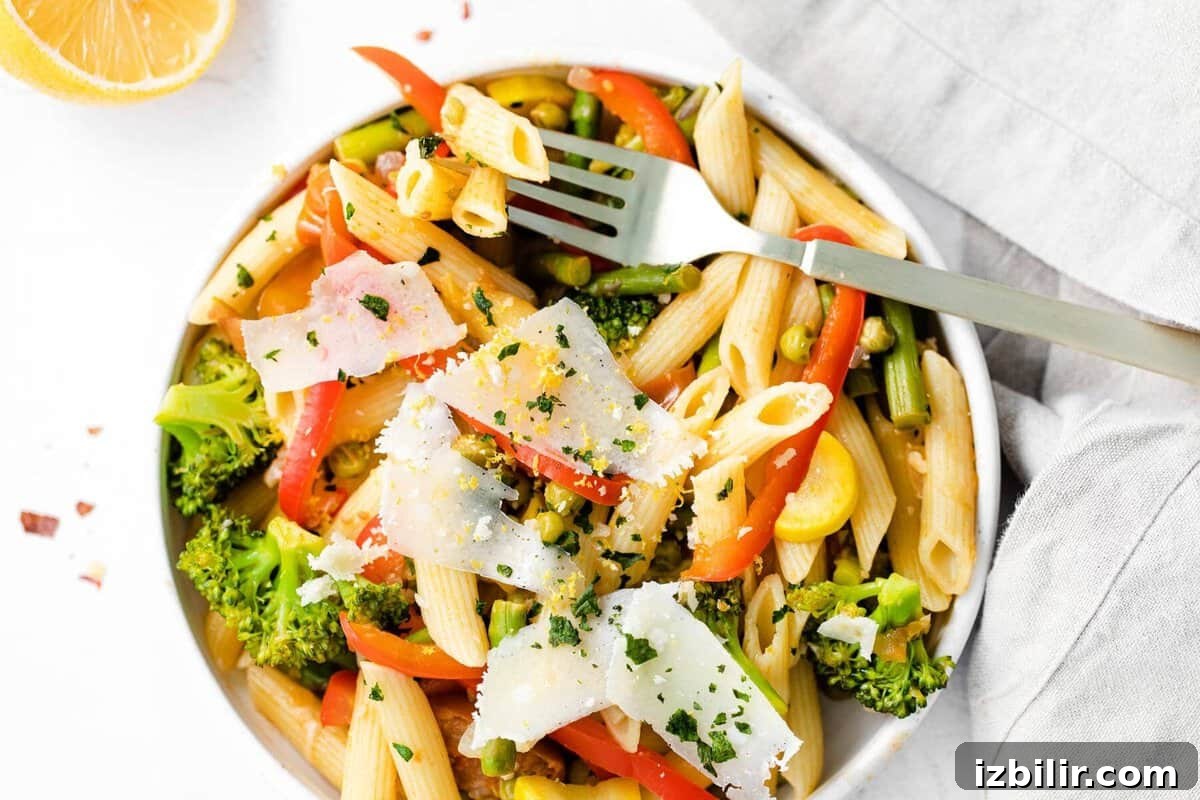 pasta primavera in a bowl topped with parmesan cheese and fresh basil